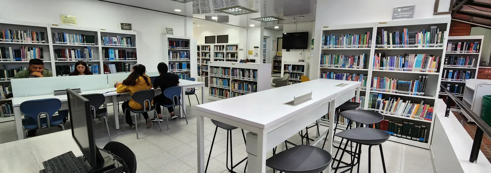 Biblioteca moderna con estanterías, mesas de estudio y personas leyendo o trabajando.